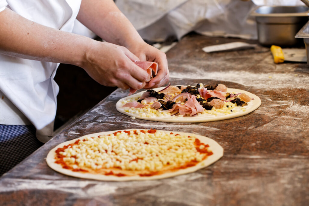 Cook putting toppings on two pizzas.